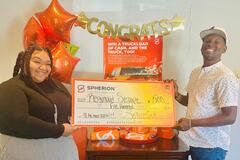 A Spherion female employee helps a Spherion Works Sweepstakes winner hold up a giant $500 check